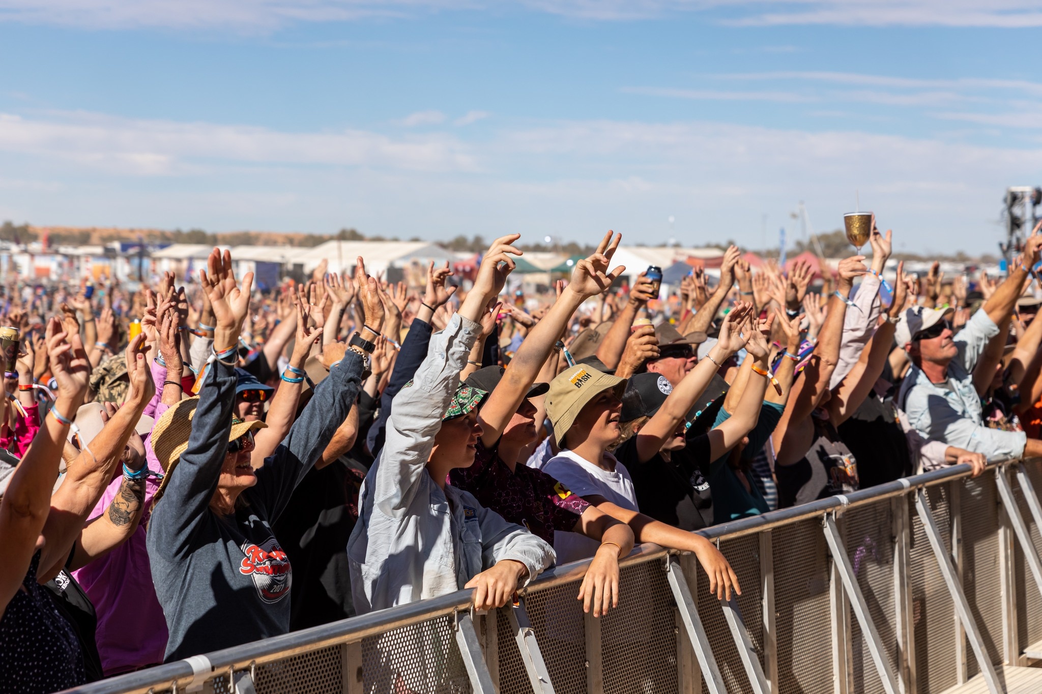 A crowd of people standing against the railing cheering at a concert.