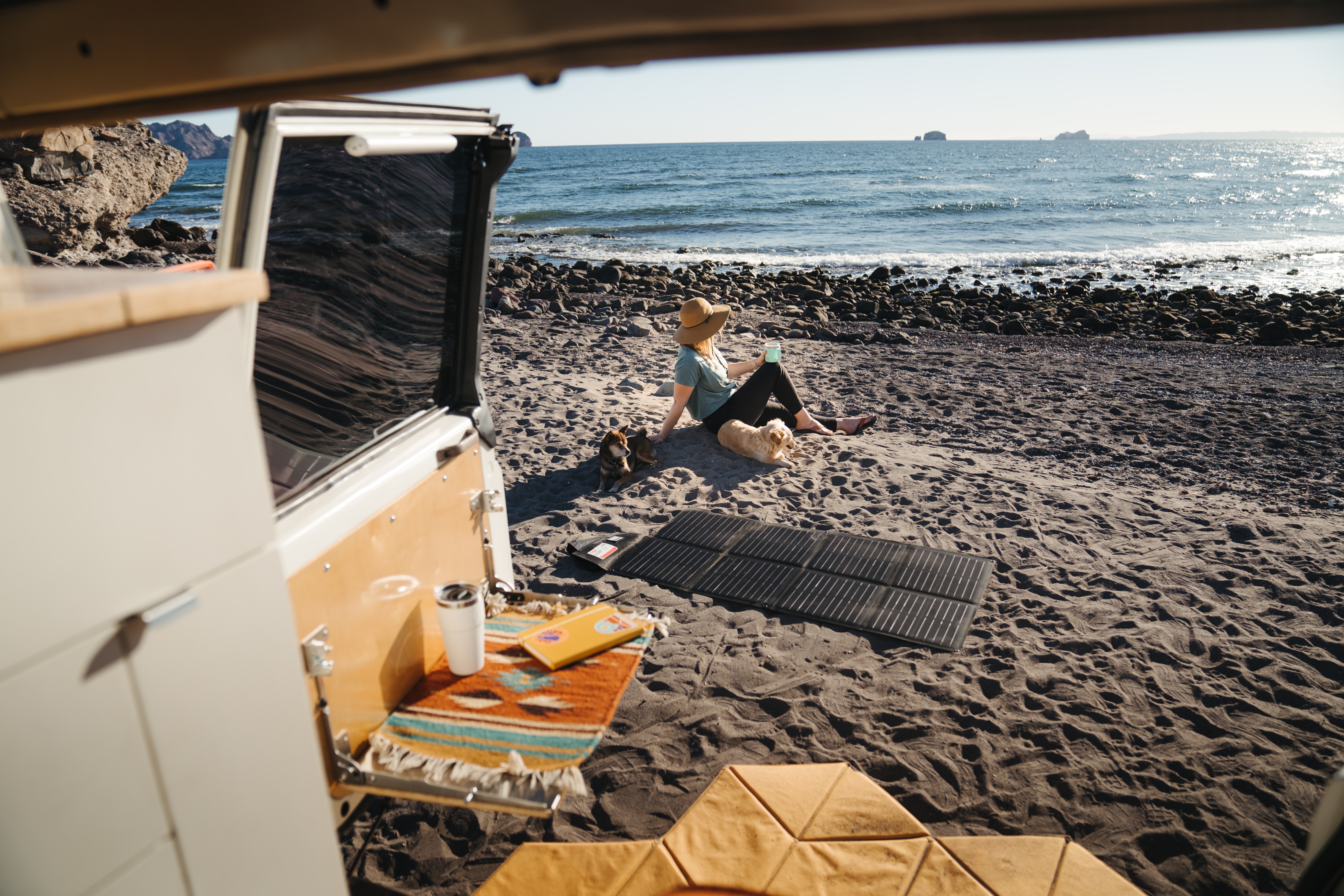 A woman sitting on the beach next to a solar blanket 