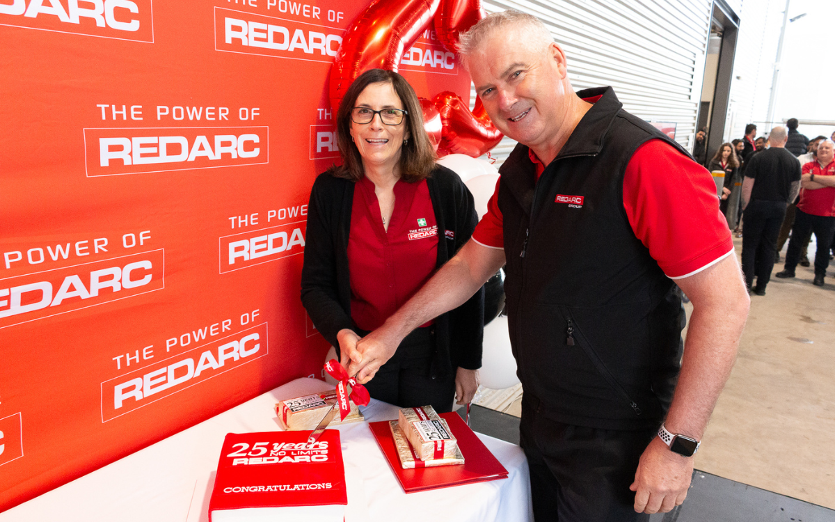 Anthony and Michelle Kittel, REDARC's owners, smiling and cutting a cake in front of a REDARC branded wall.