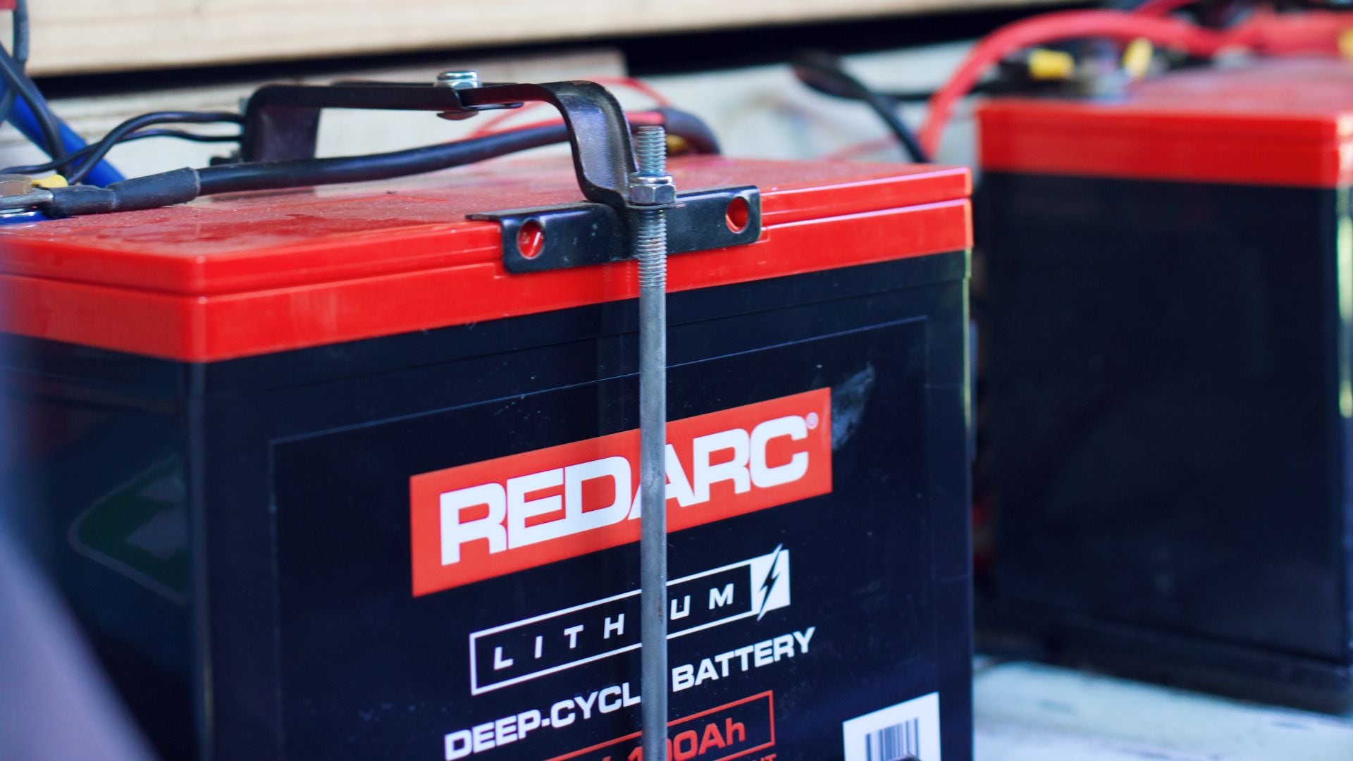 Close-up of a REDARC Lithium Alpha 150 battery secured inside a vehicle, with camping gear visible in the background