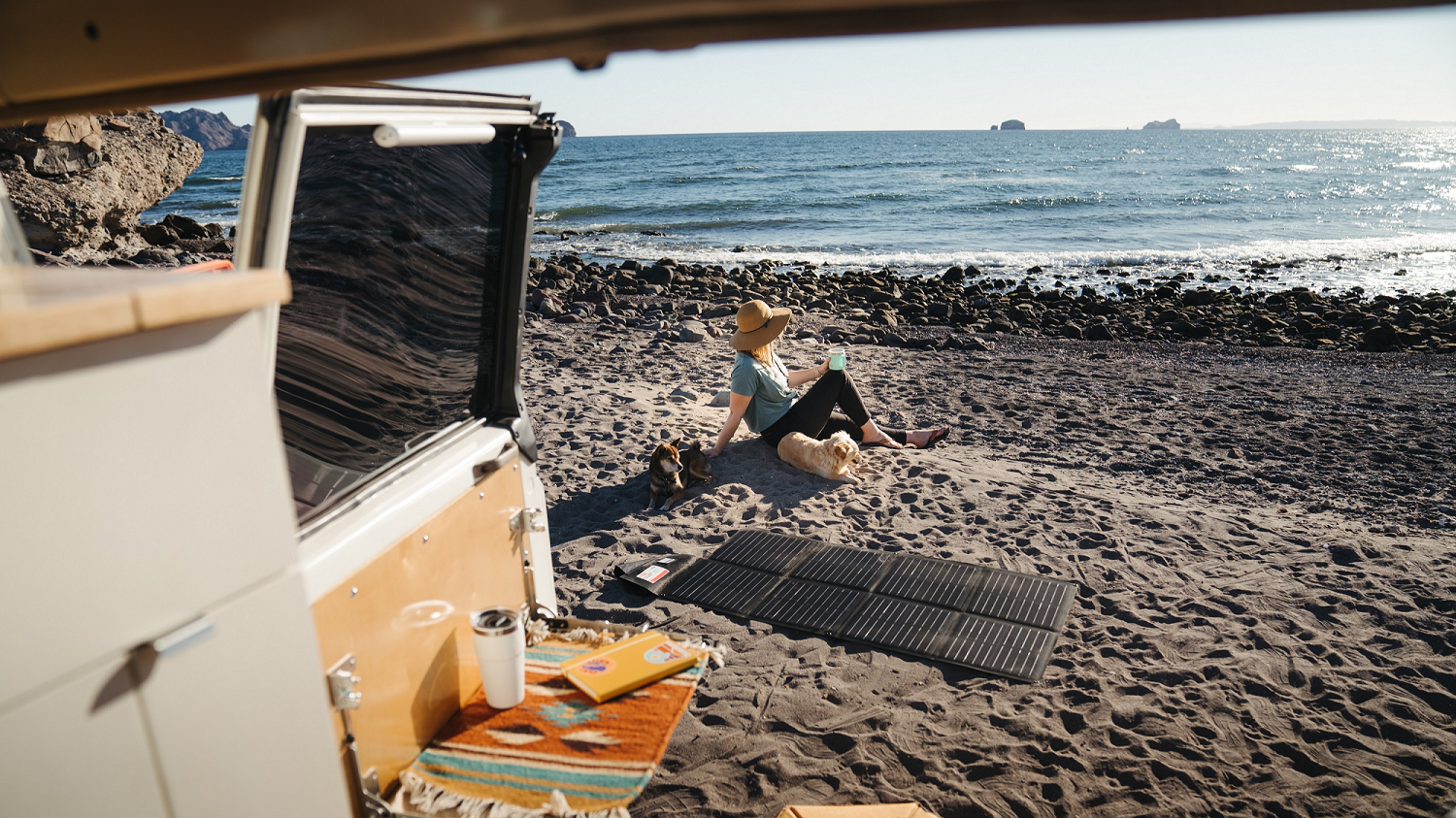 A woman sitting on the beach next to a solar blanket 