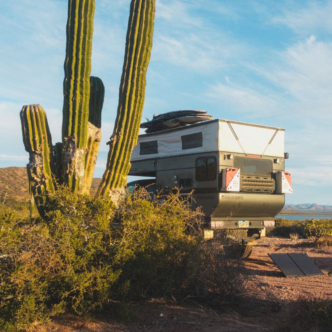 Off-road vehicle with pop-up camper parked by a cactus in a desert, with a clear blue sky in the background Off-road vehicle with a pop-up camper parked next to a large cactus in a desert landscape under a clear blue sky